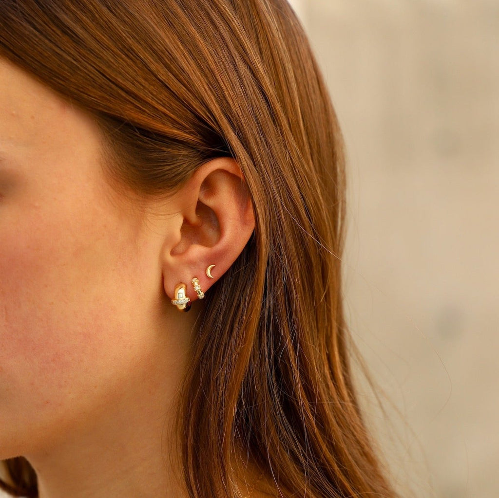 Add a touch of sparkle to your basic gold hoops with our Eva Mini Hoops. These mini hoop earrings feature three sparkling CZ rings, providing timeless glamour to any look.