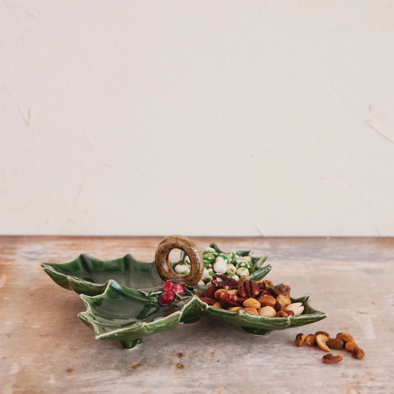 Green ceramic dish shaped like a holly leaf with snacks on a wooden surface.