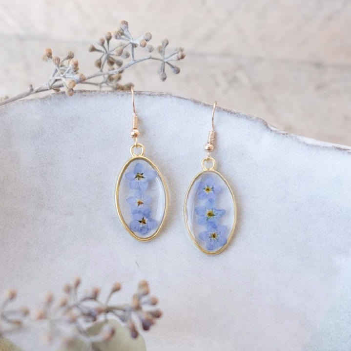 gold colored earrings featuring ovals with 3 blue forget me not flowers 