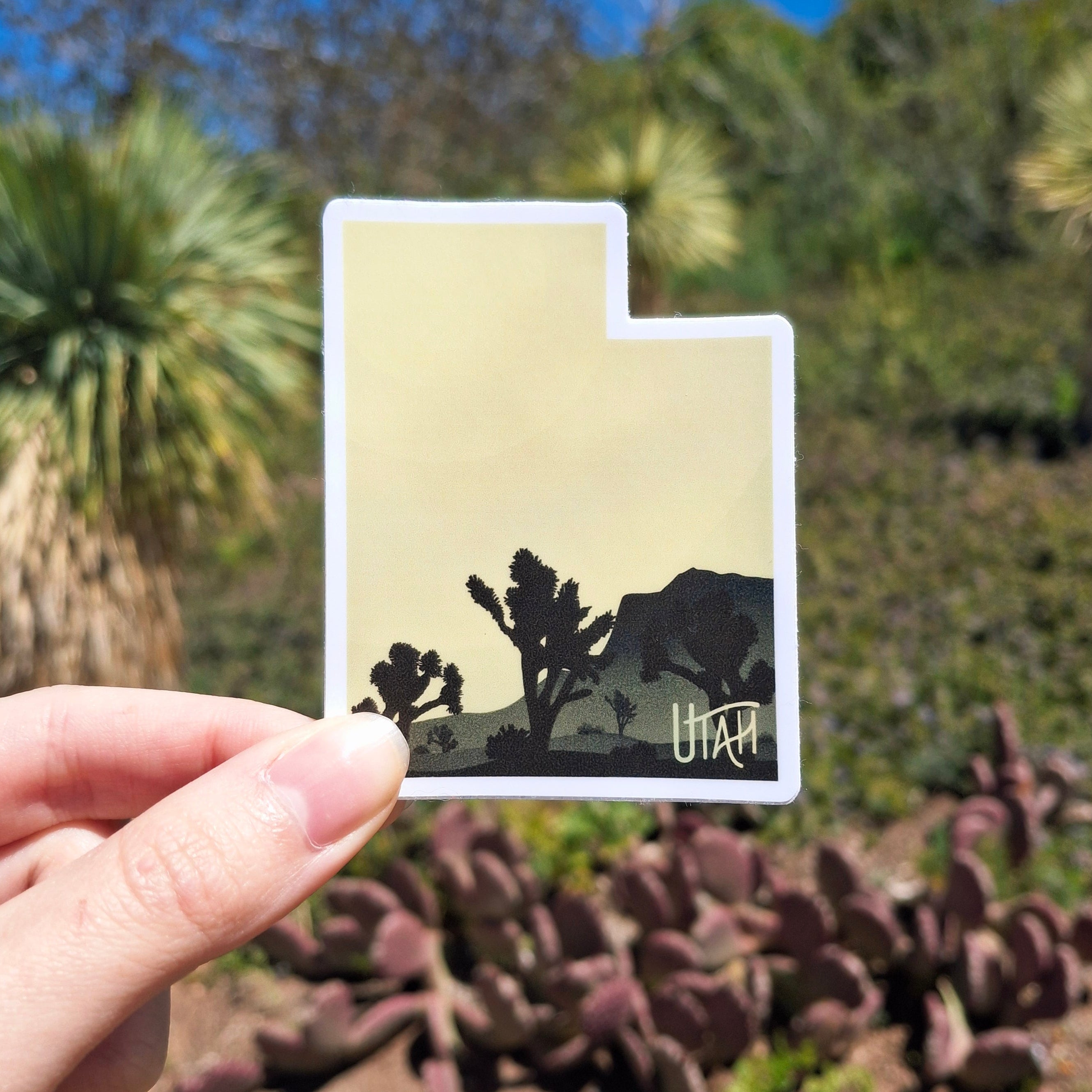 A yellow sticker in the shape of the State of Utah with black silhouettes of Joshua trees. 