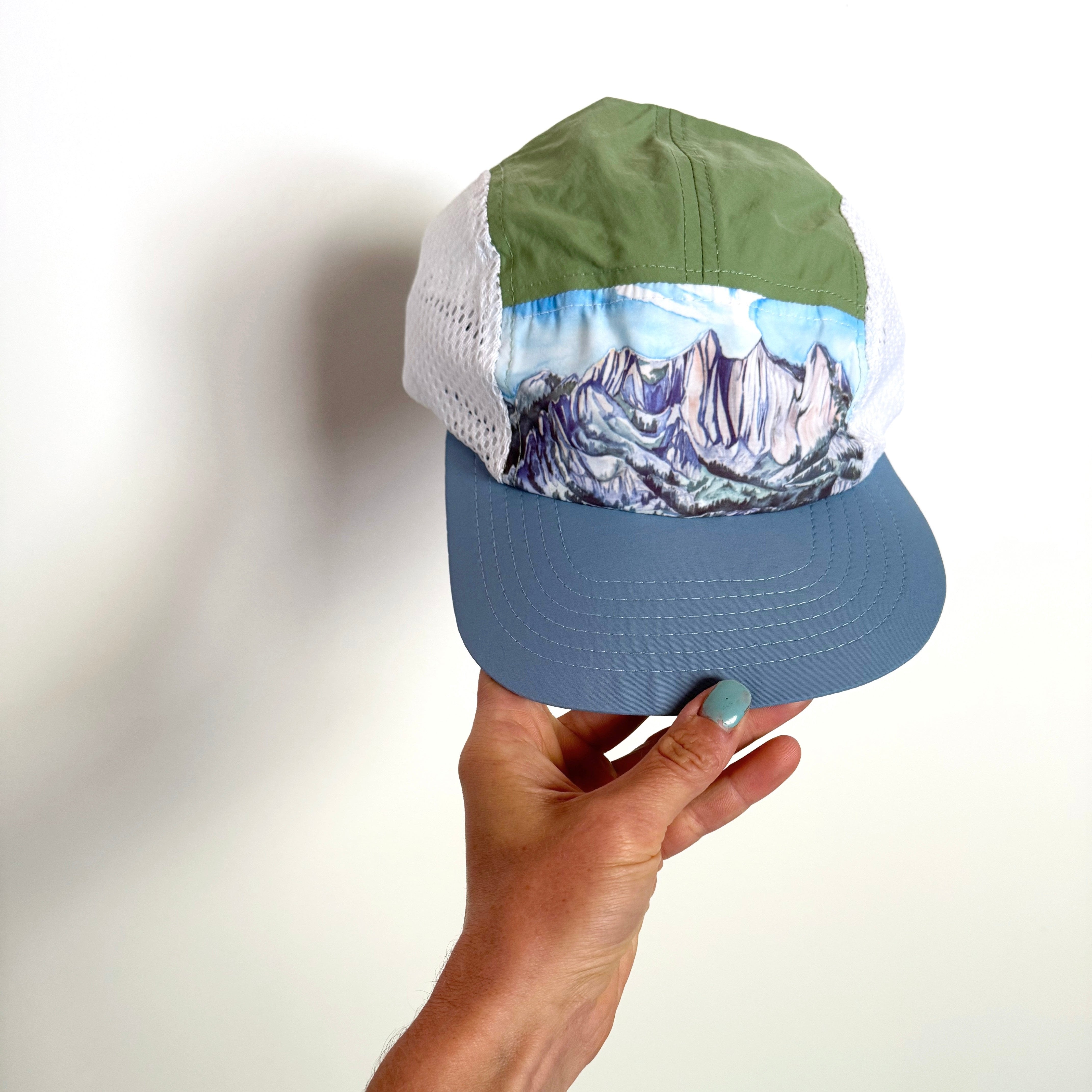 Light blue and green snap back running hat featuring a painting of lone peak