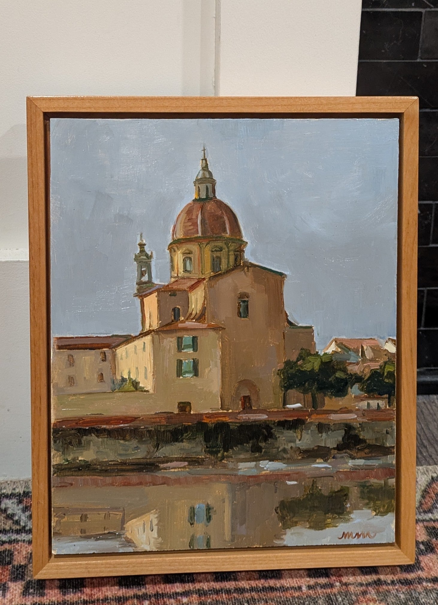 A church with a dome and a steeple, red roofs, stucco, and many windows on a water's edge. The water is still and reflects the church. The sky is dusky and pale blue. 