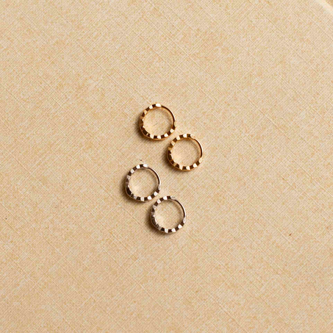 Two pairs of honeycomb huggie earrings. One pair is gold and one is silver. They are both lying on their side on a linen surface. 