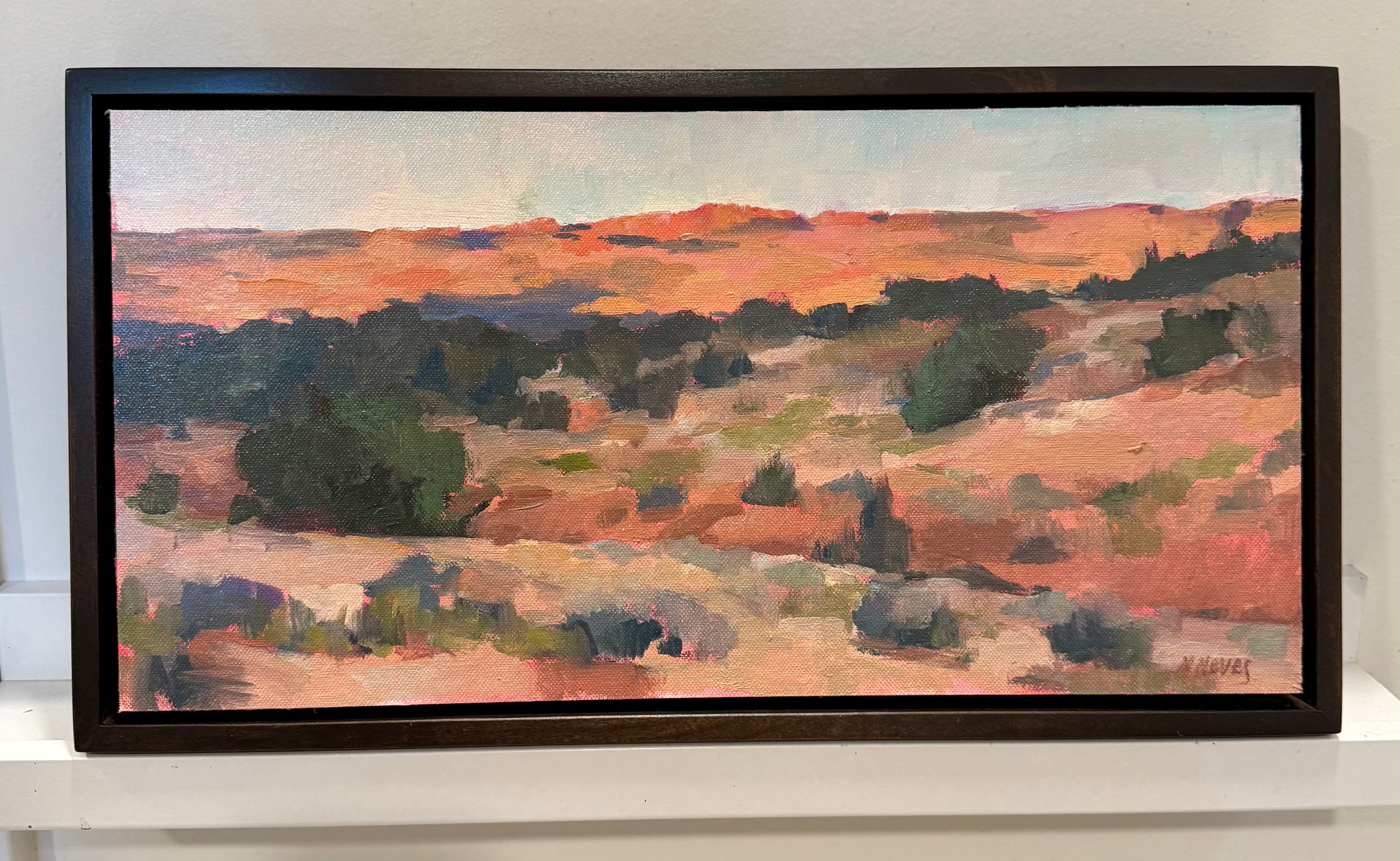 Red rock desert at dusk. Rolling hills of the red dirt with scattered greenery at dusk. The sky is pale blue with hints of pink and the landscape is a mix of hues of red, pink, purple, and orange. 