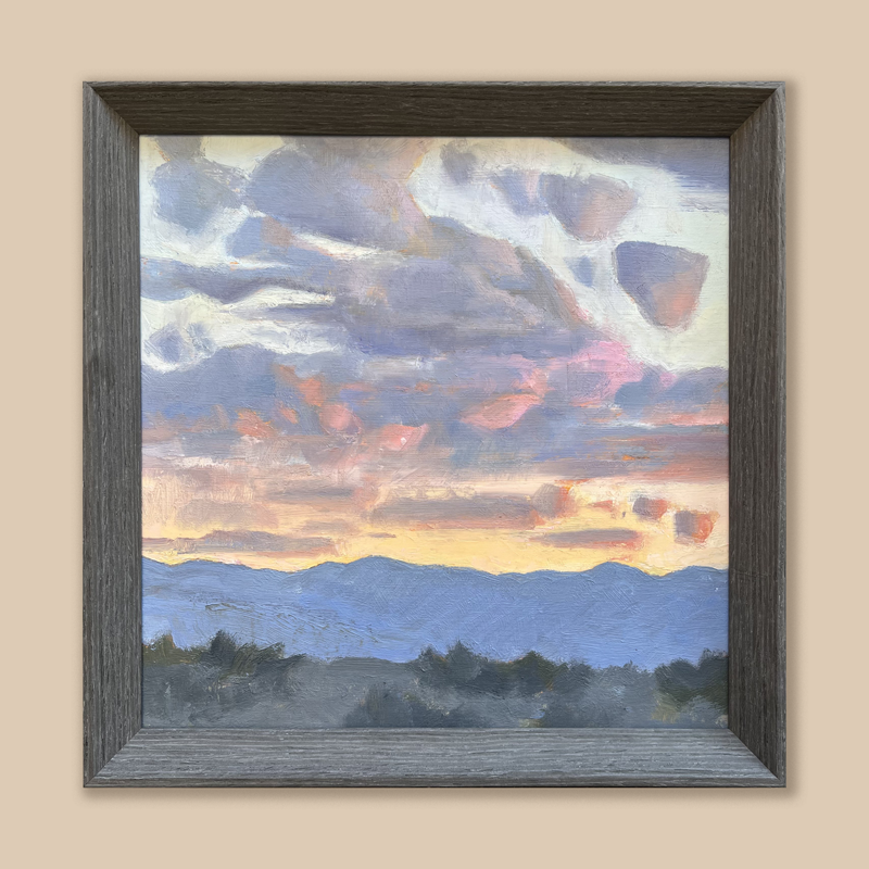 A gray frame surrounding the painting of a yellow, pink, and blue sky over a blue mountainscape. 