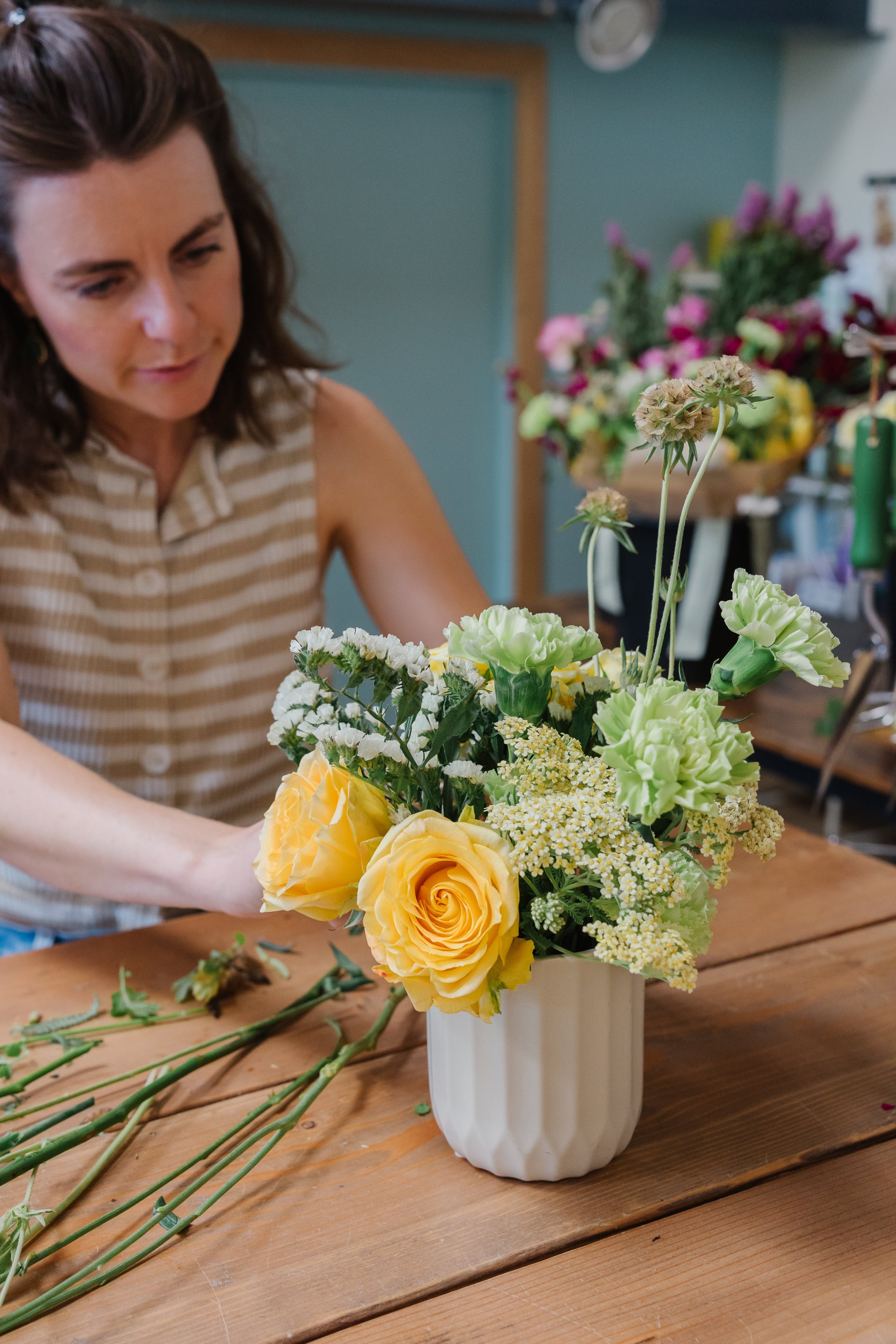 Woman arranging flowers in a vase on a wooden table