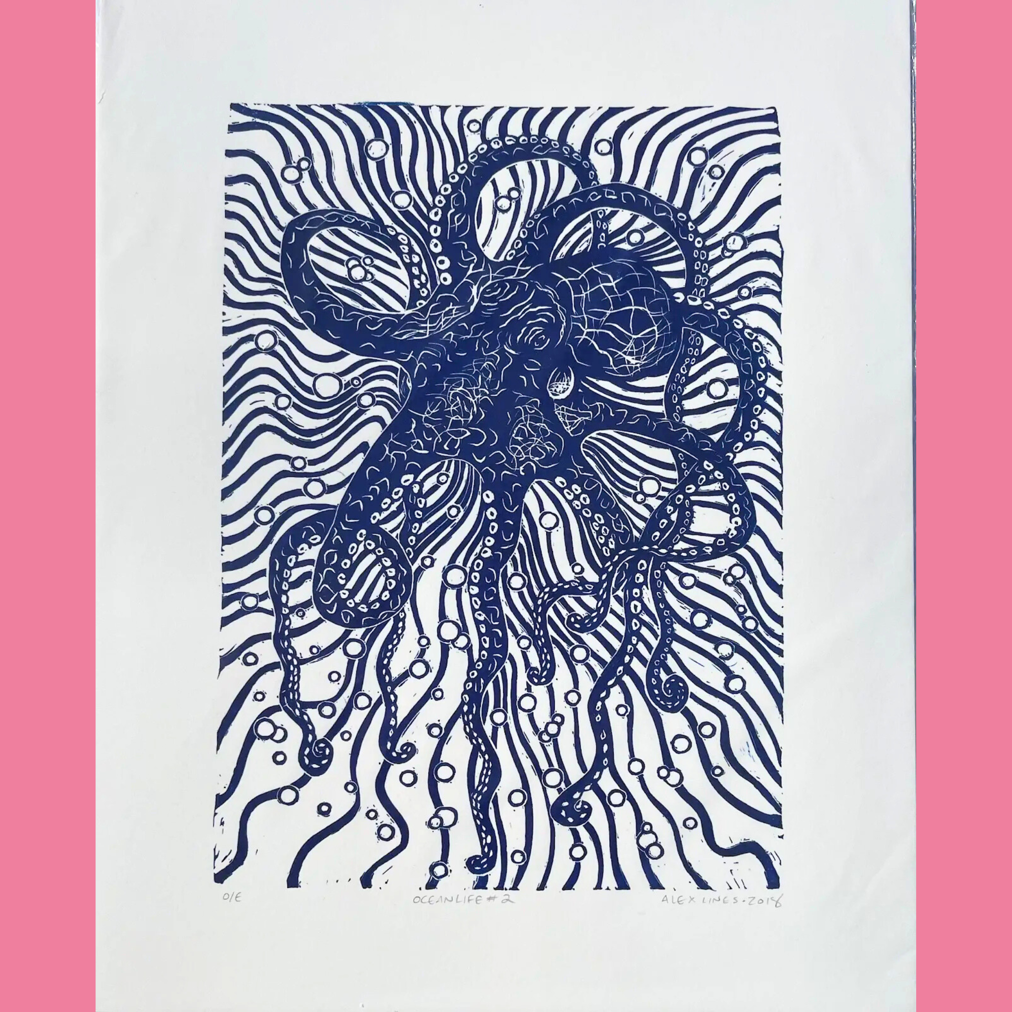 A black-and-white linocut print features a large, intricate octopus centered in the composition, with its eight curling tentacles spreading outward amid swirling, wavy lines representing ocean currents and numerous white circular bubbles rising throughout the scene. The artwork is printed on white paper with the title "OCEANLIFE #2," the number "016," and the signature "ALEX LINES • 2016" written below, surrounded by a bright pink border.