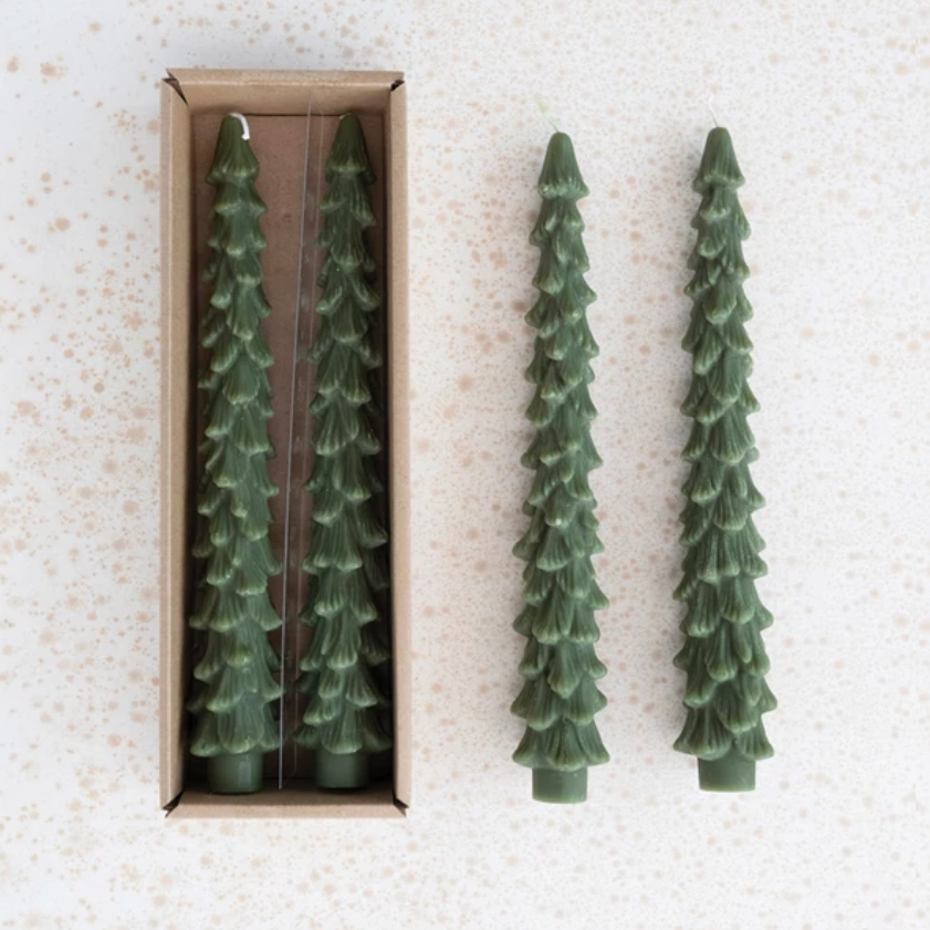 Two green tree-shaped candles on a textured white surface with one candle out of the box.