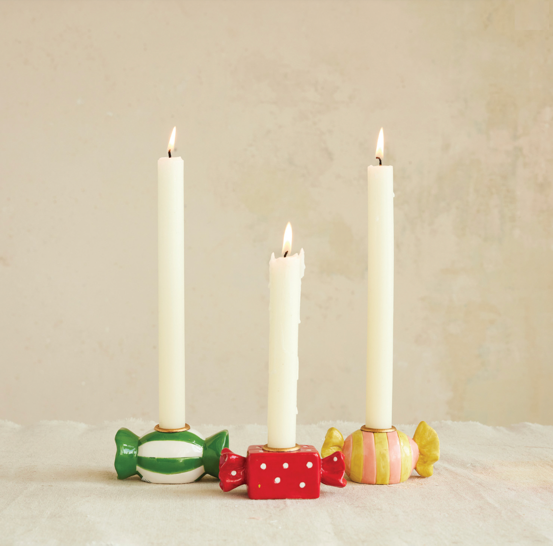 Three candles in colorful holders on a textured surface with a neutral background