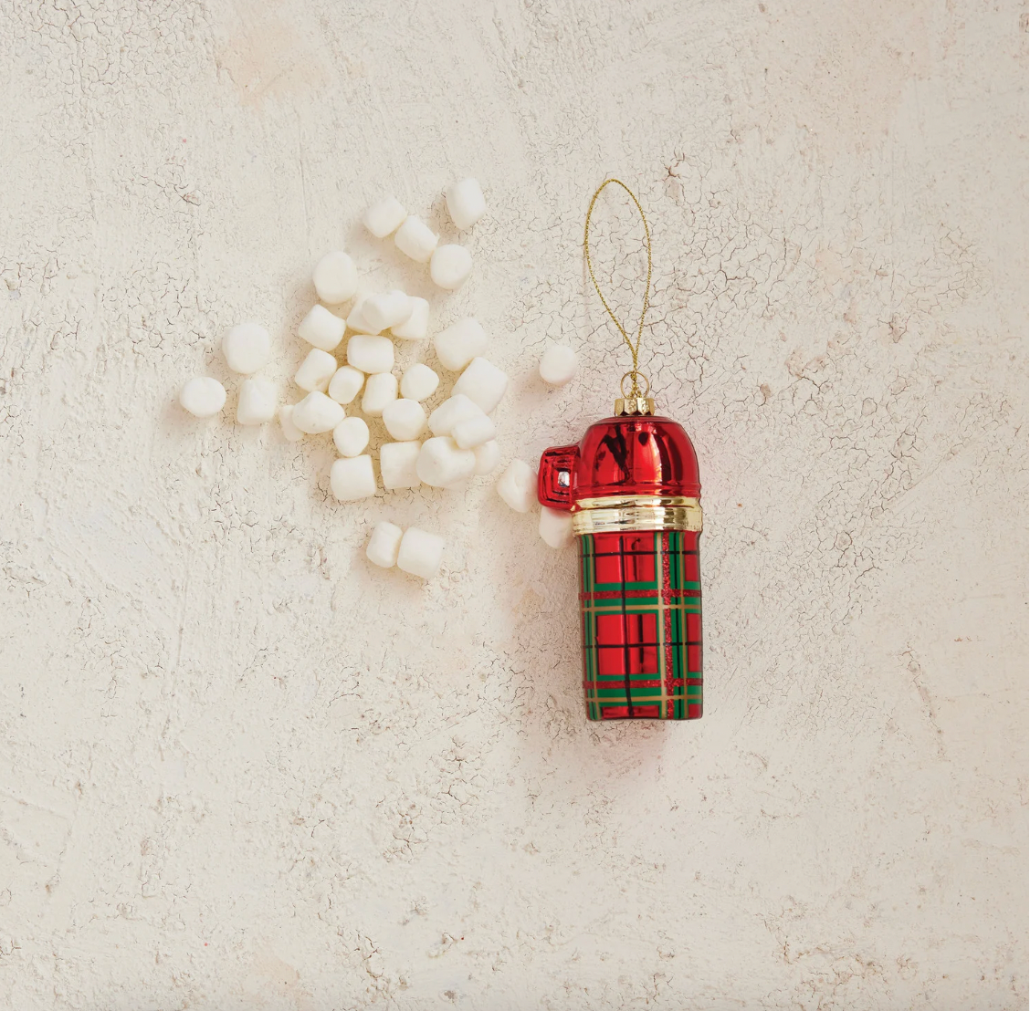 Red and green plaid thermos ornament with marshmellows on a textured beige background