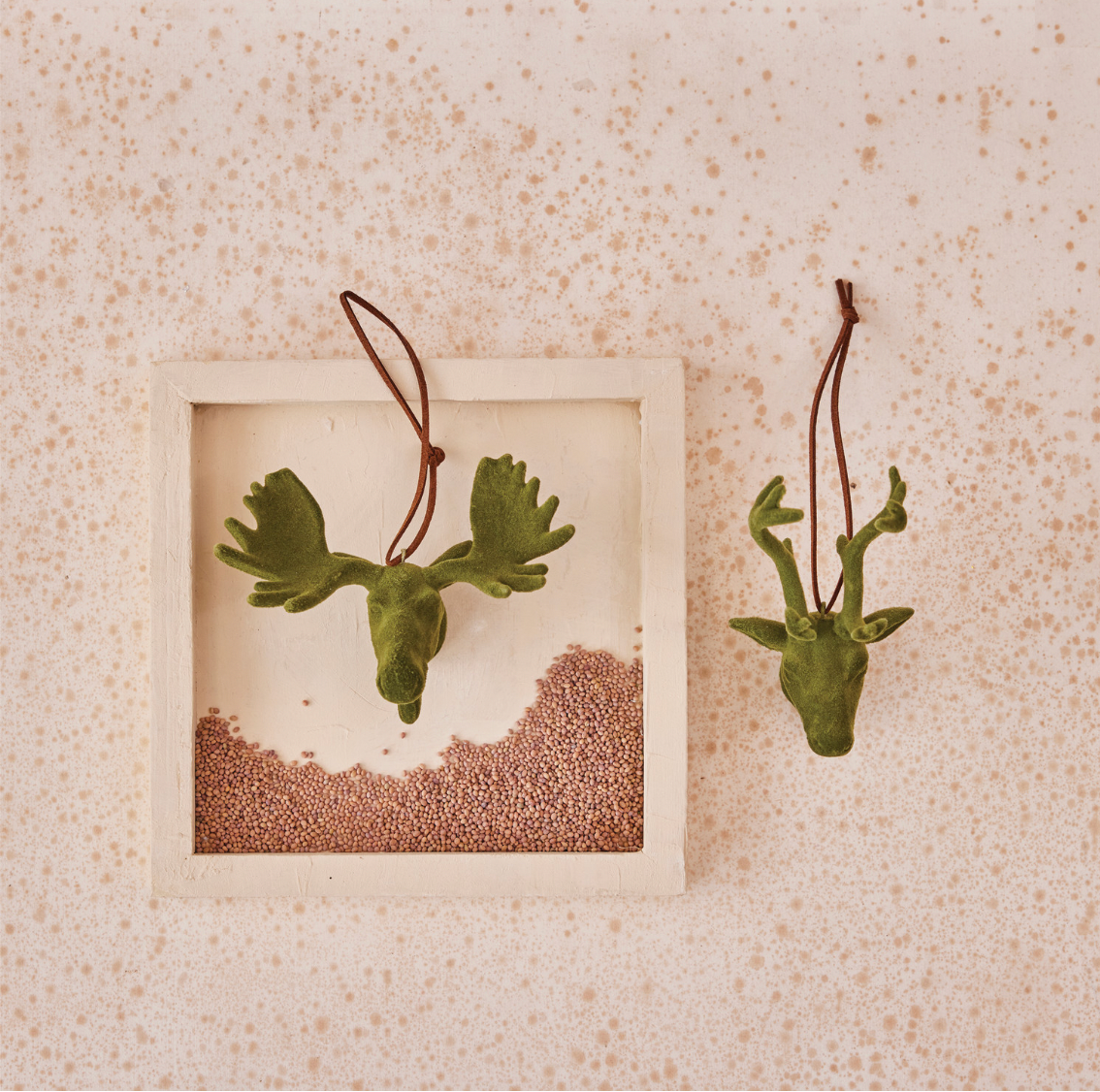 Green deer head  & moose head ornaments hanging on a textured beige wall.