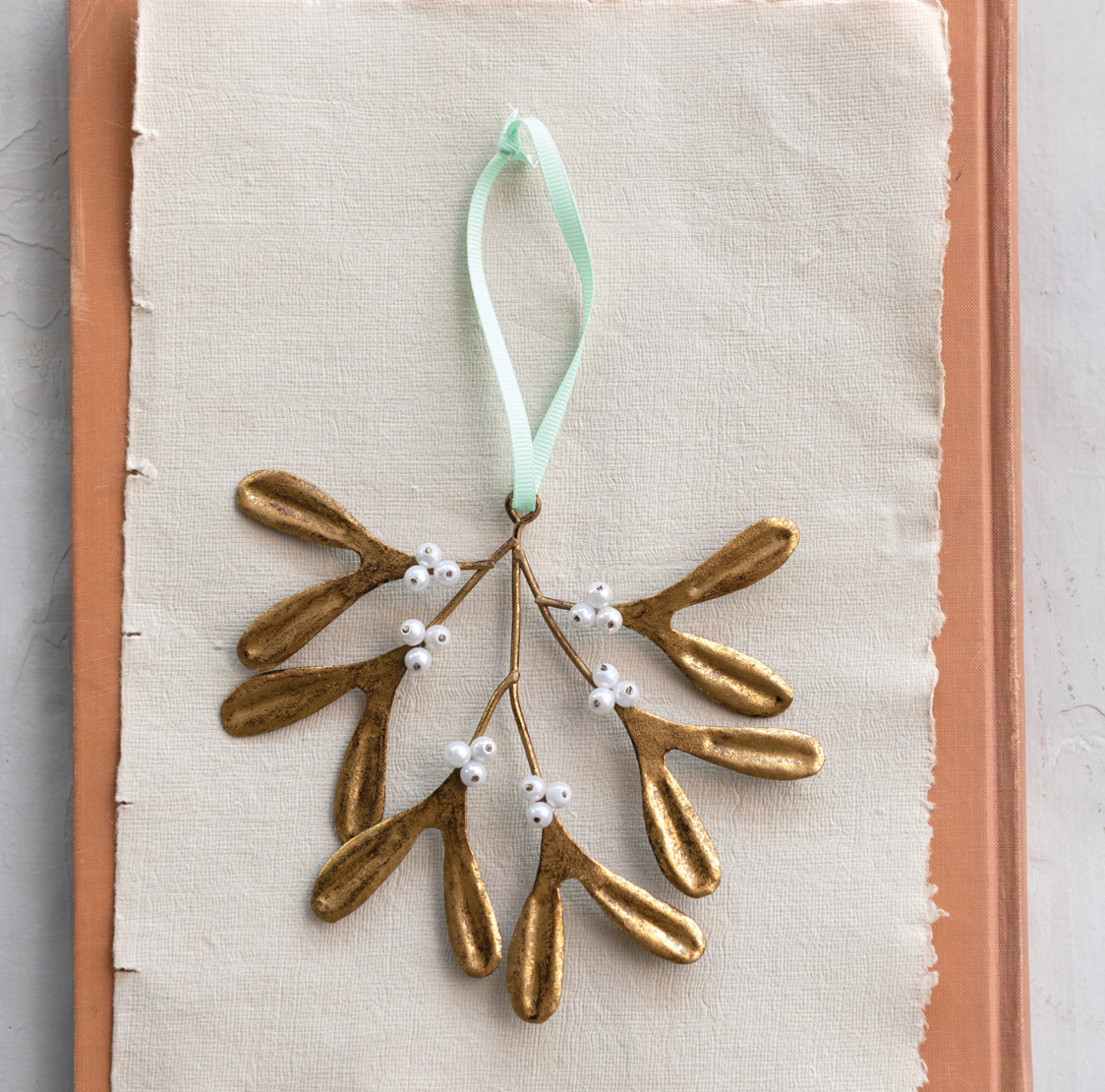 Decorative gold mistletoe ornament with white berries on a light fabric background
