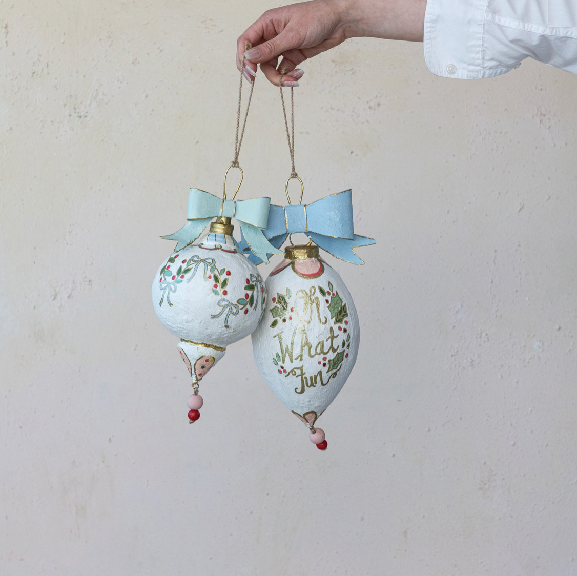 Two decorative Christmas ornaments with ribbons against a plain background