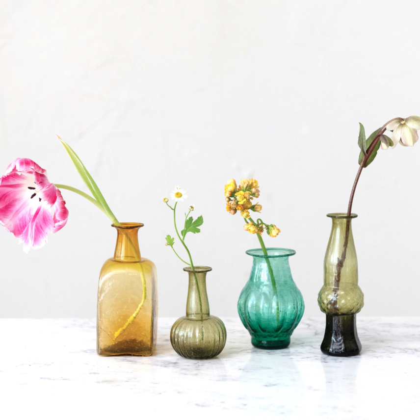 Four glass vases of different colors with flowers on a light background