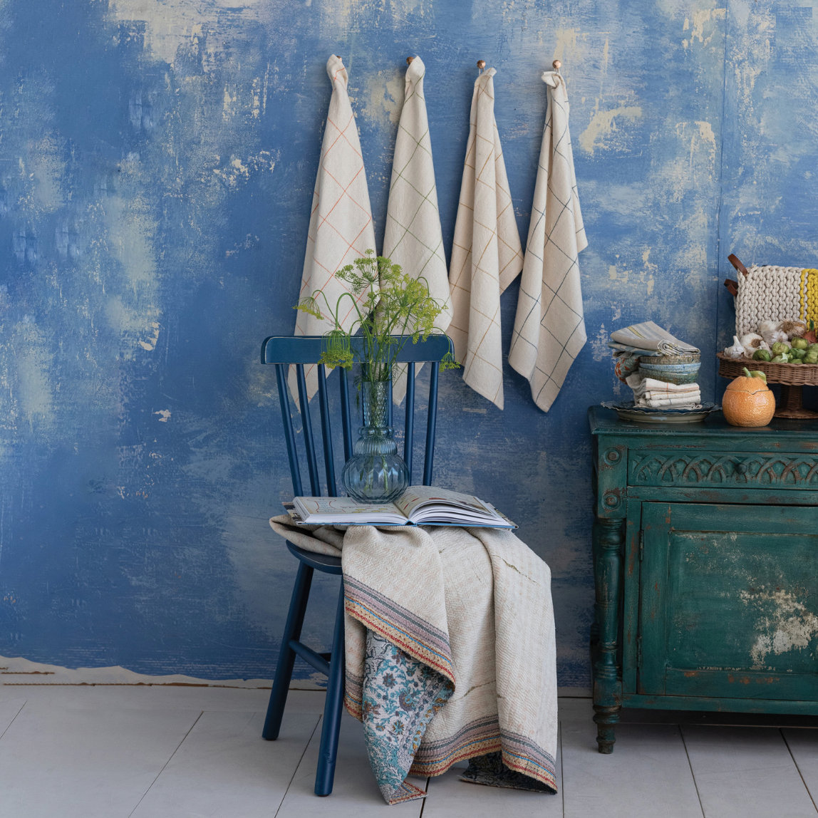 Decorative setting with a blue wall, chair, and table with books and a vase.