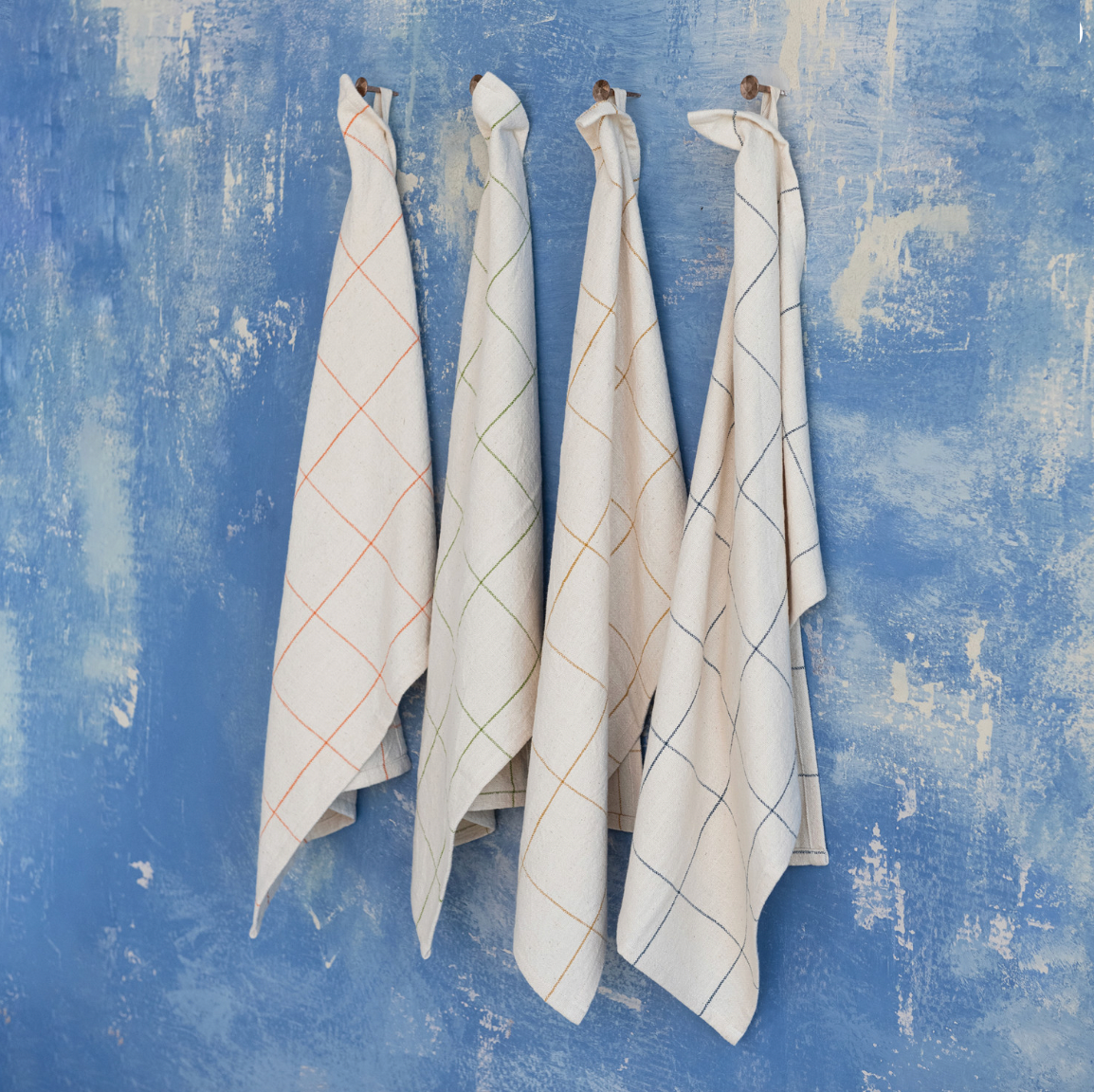 Four patterned towels hanging against a textured blue wall.