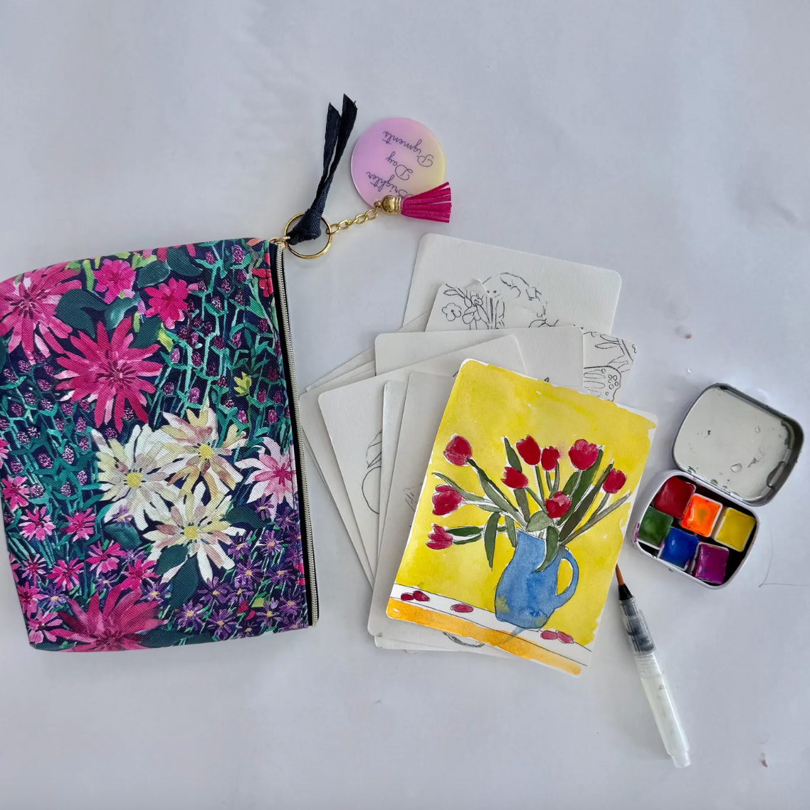 Floral pouch, watercolor painting, cards, and art supplies on a white background