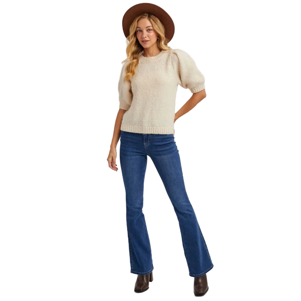 Woman wearing a beige sweater, blue jeans, and a brown hat on a white background