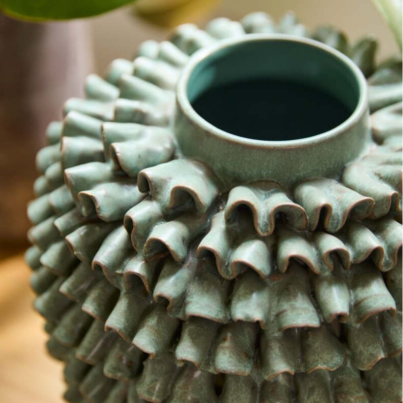 Textured ceramic vase with a central opening on a wooden surface
