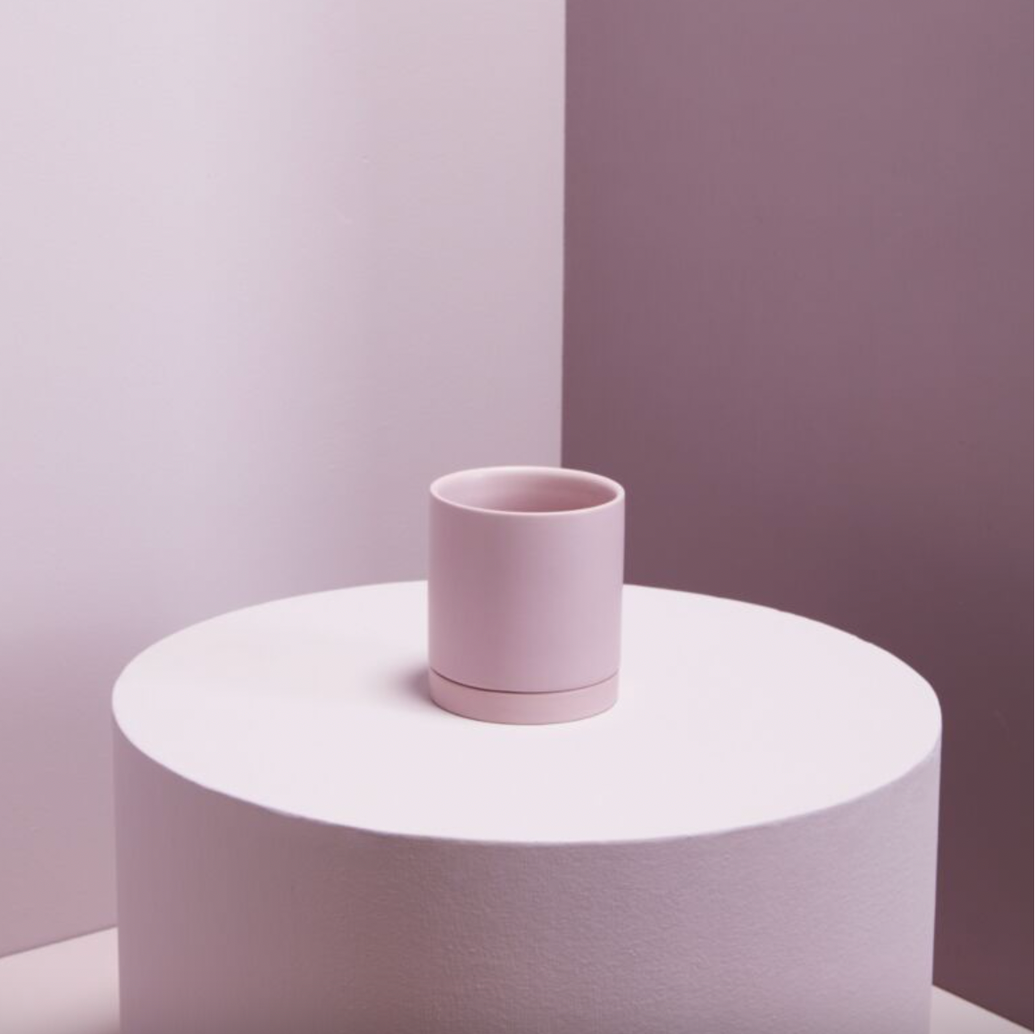 Pink ceramic cup on a white pedestal against a two-tone wall.