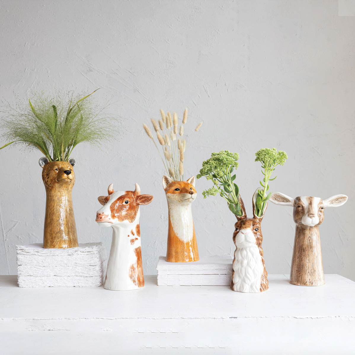 Set of animal-shaped vases with plants on a white surface and light gray background