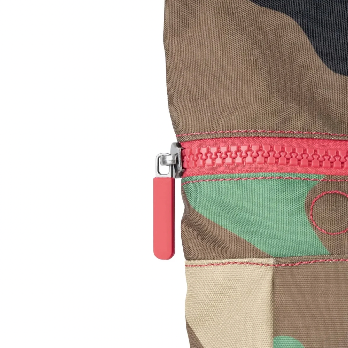 Close-up of a camouflage fabric bag with a bright pink zipper and matching pink zipper pull on a white background.