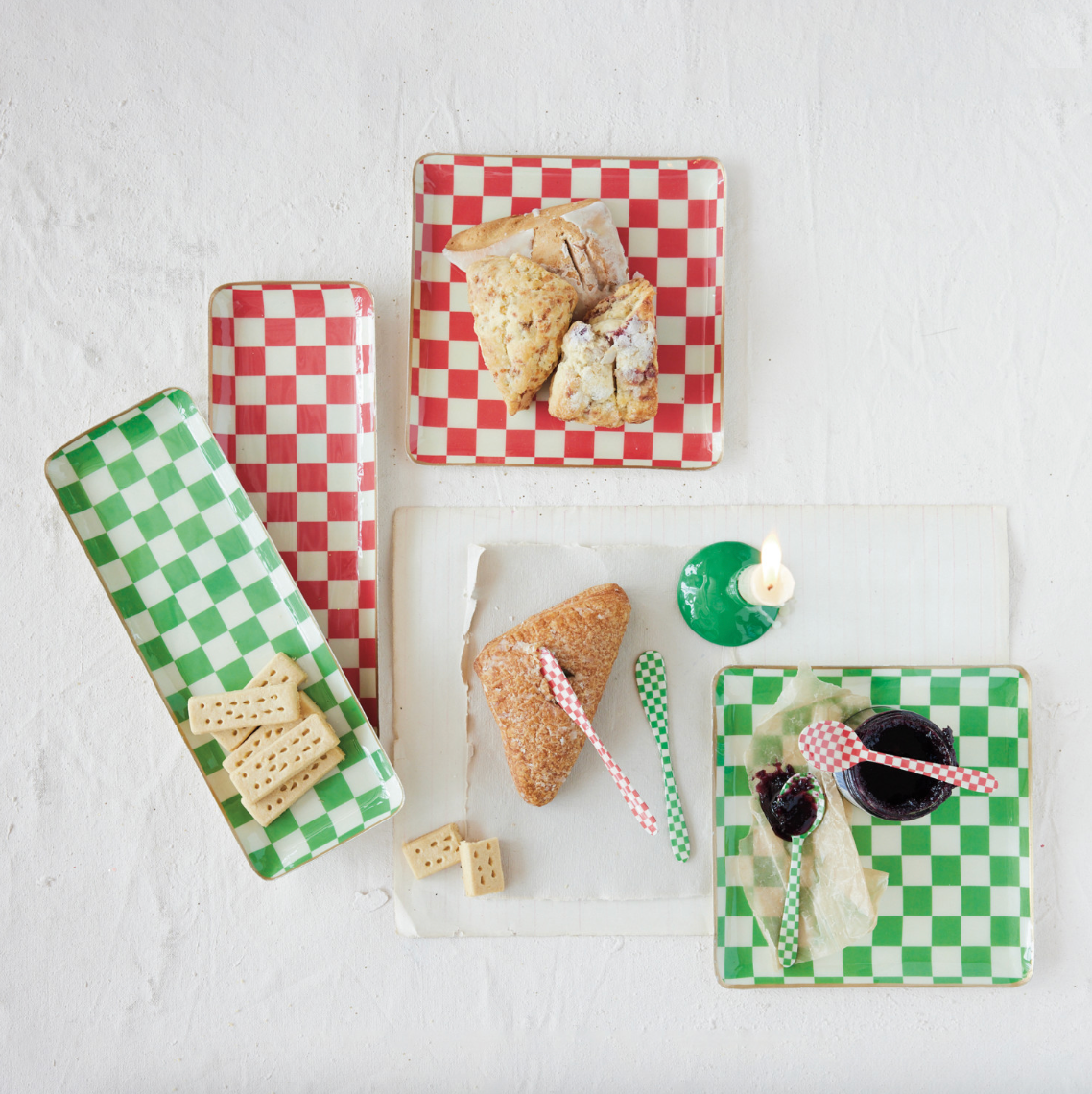 A styled flat-lay of red and green checkered rectangular ceramic plates with matching cutlery, holding scones and a small green cup, arranged on a white textured background.