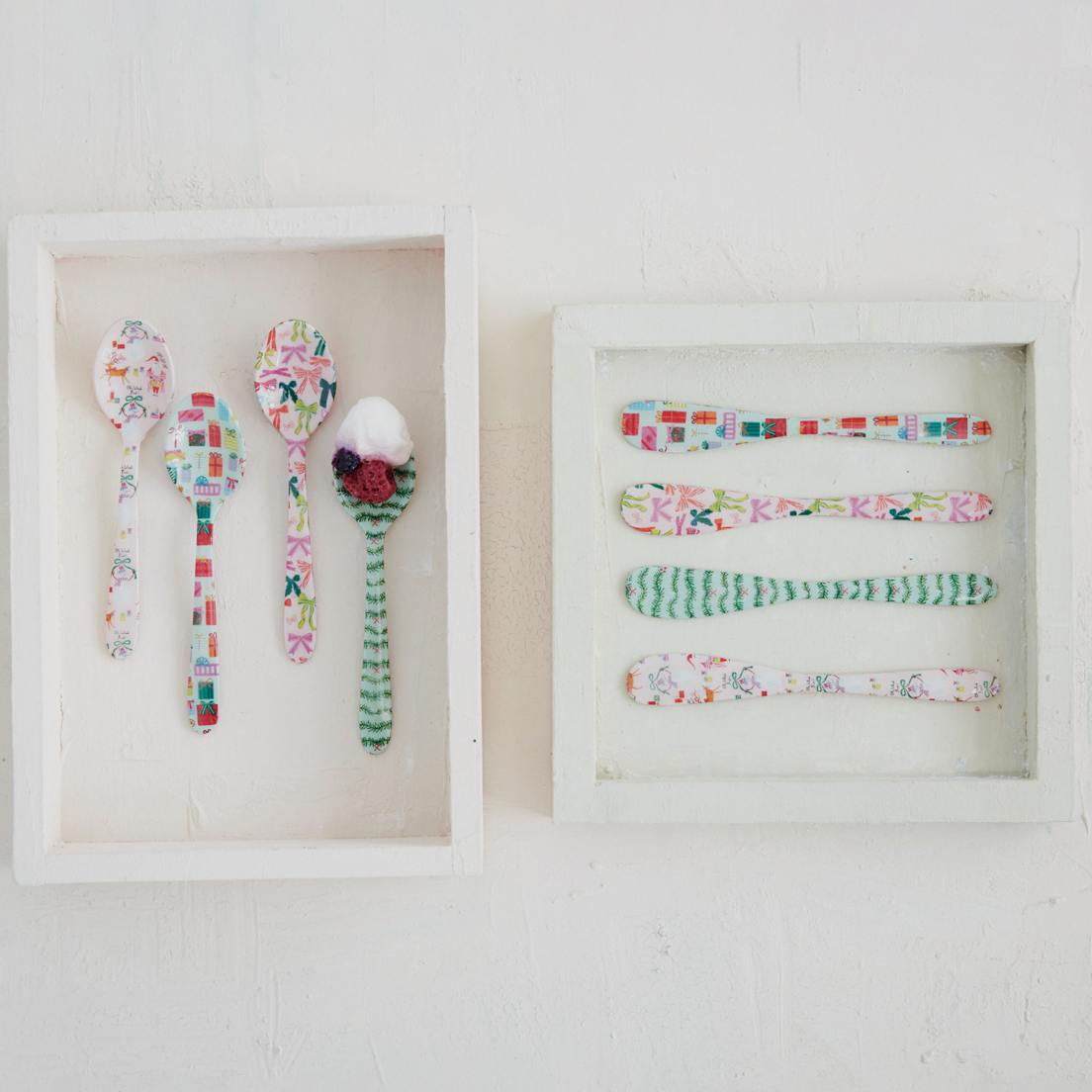 Two white square shadow-box frames mounted on a white wall, each holding multiple decorative spoons with colorful floral, geometric, and striped patterns.