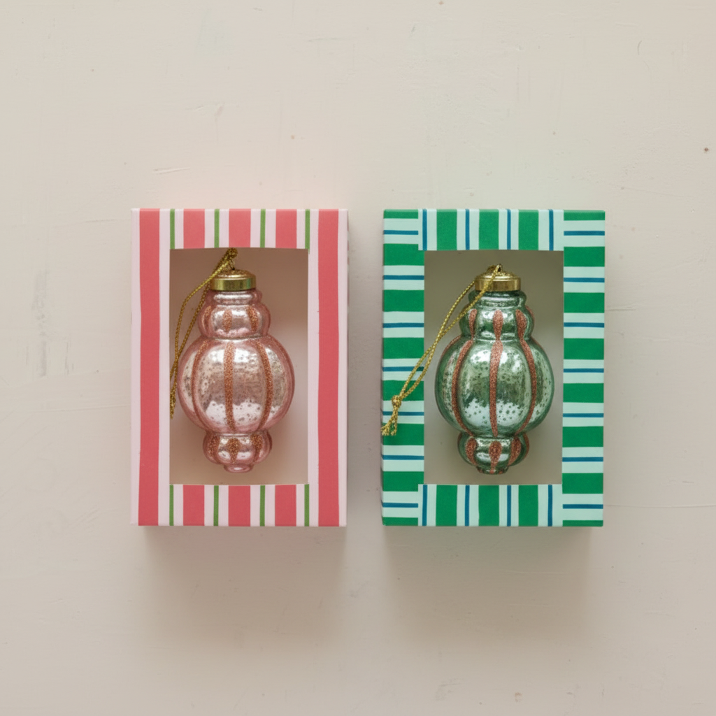 Two vintage-style glass ornament hangings displayed side by side on a light beige wall. The left hanging features a pink ribbed glass ornament with a gold cap and green one.