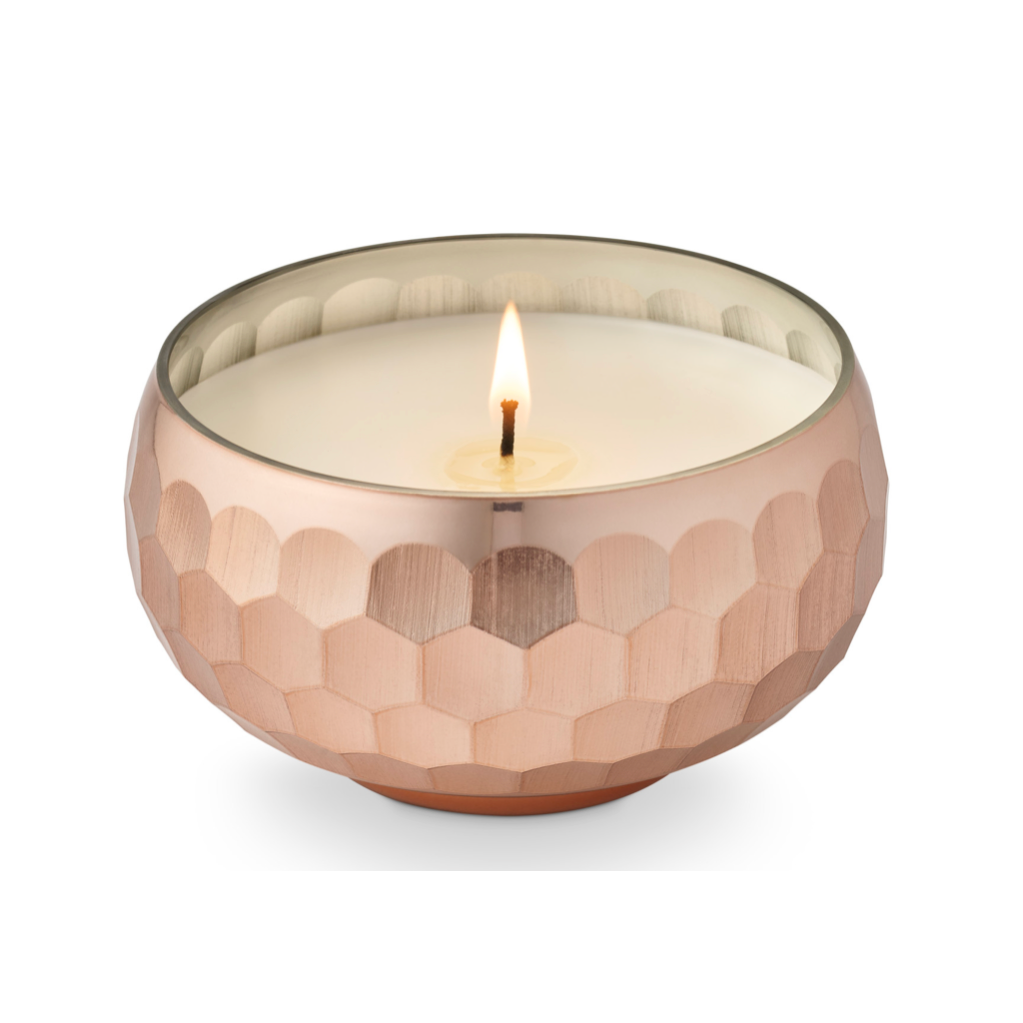 A lit single-wick candle in a hammered metallic rose-gold bowl with a clear glass rim, shown on a clean white background.