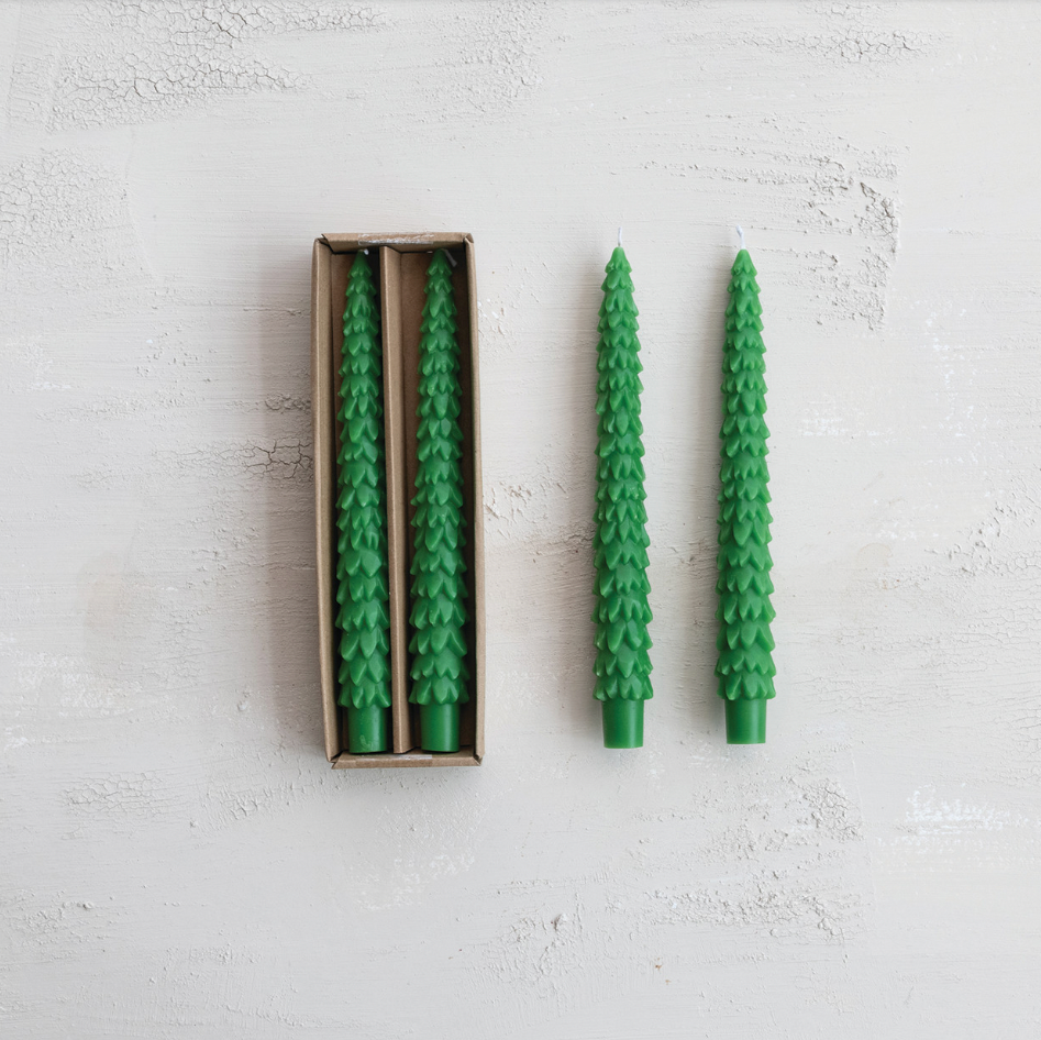 Two green tree shaped candles on a light gray surface with one candle in an open box.