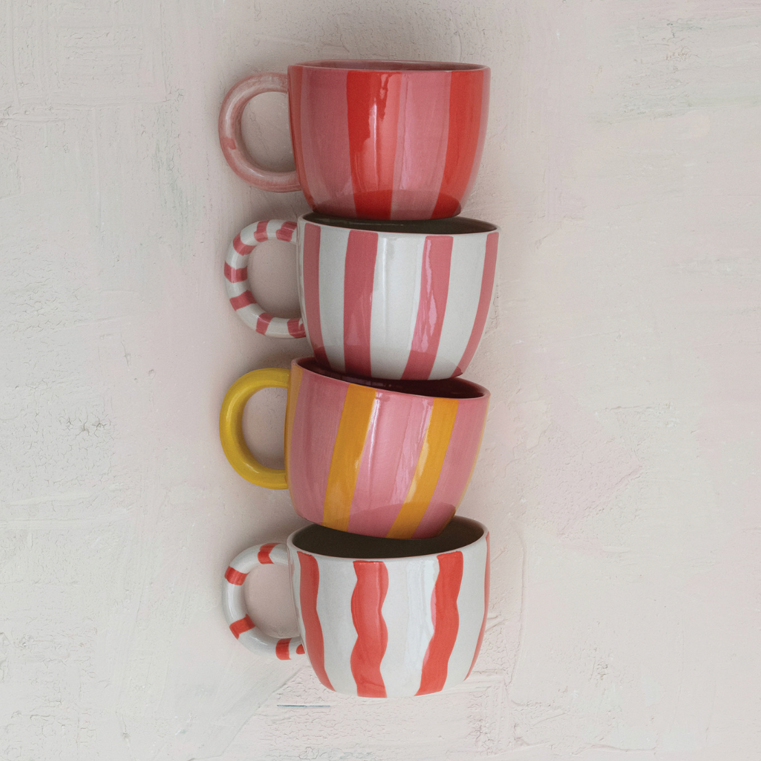 Stack of four striped ceramic cups on a light gray background