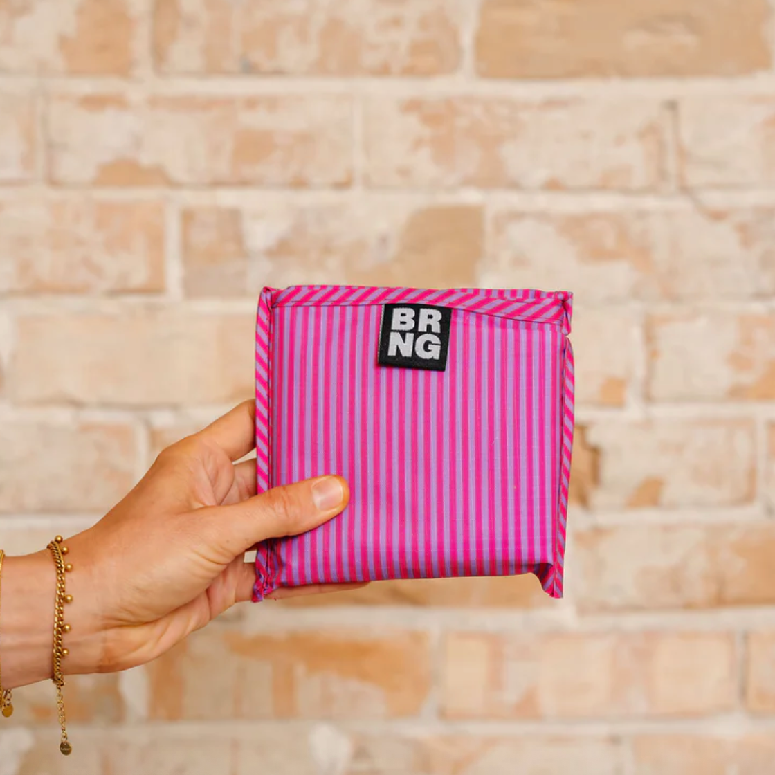 Hot pink striped tote folded neatly into a 5.5" square held in one hand. 
