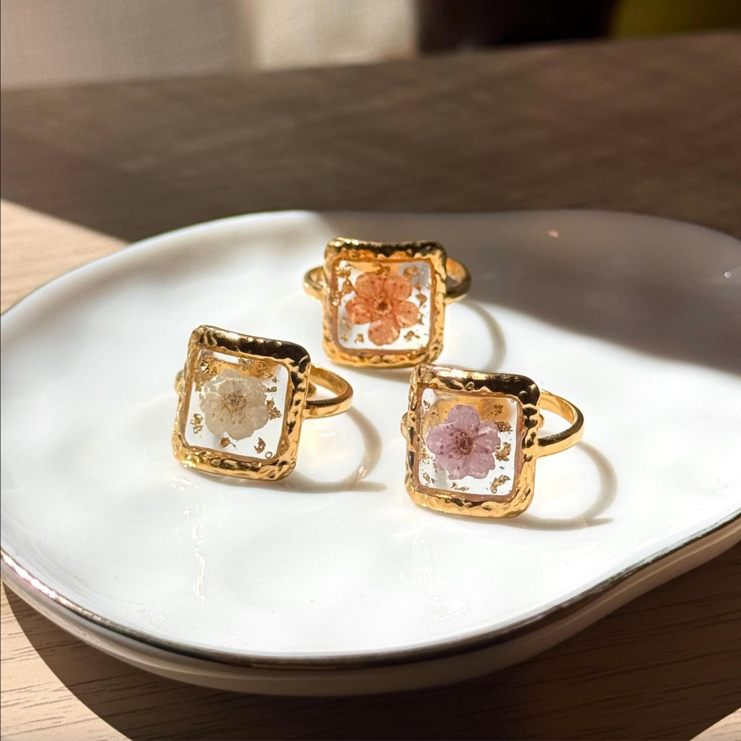 An adjustable 18k gold ring with a square center and resin filled with dried florals. 