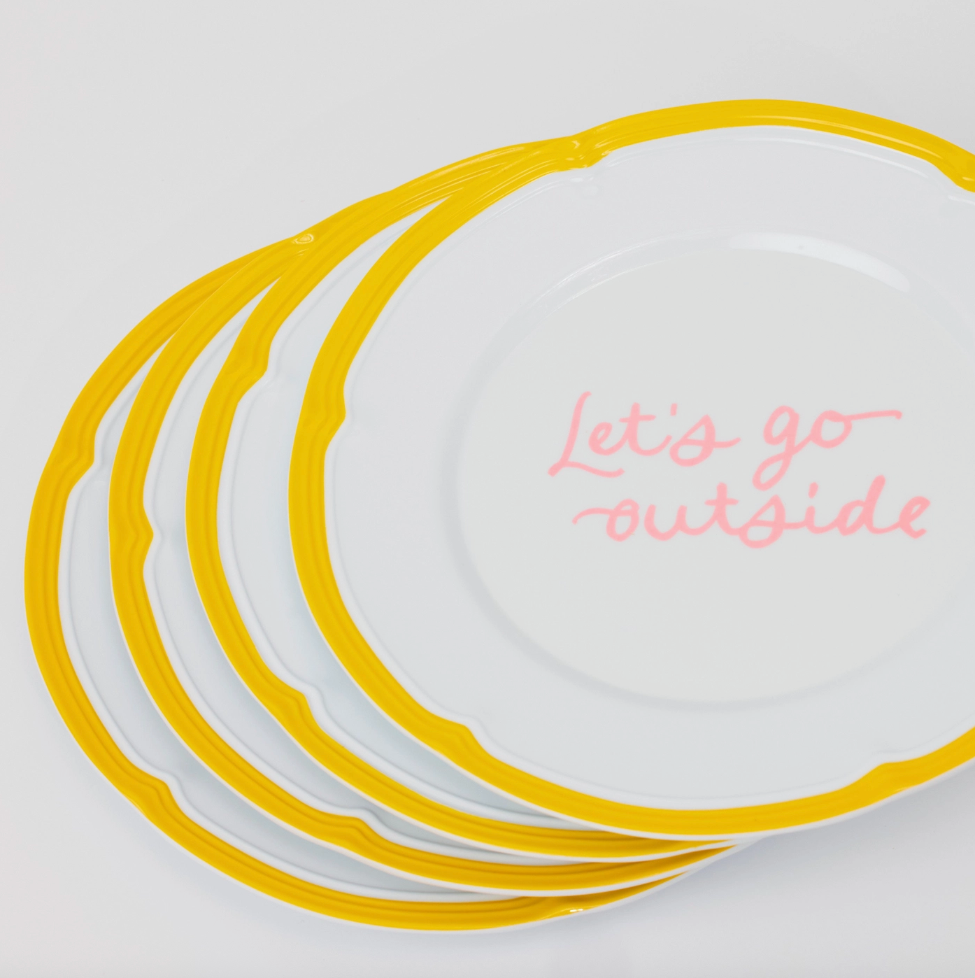 A stack of four plates slightly ajar, with a yellow border and the top plate says, "Let's go outside" in pink cursive. 