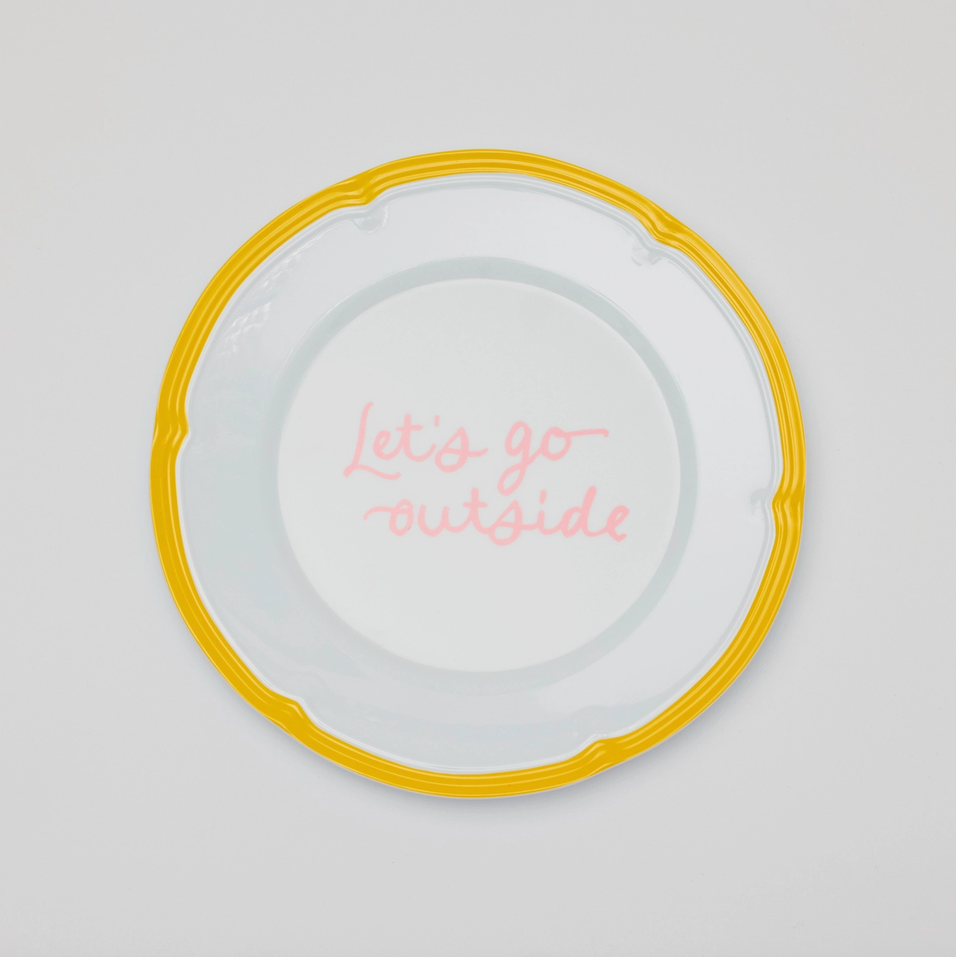 A round plate with a yellow border with "Let's go outside" written in pink cursive in the center. 