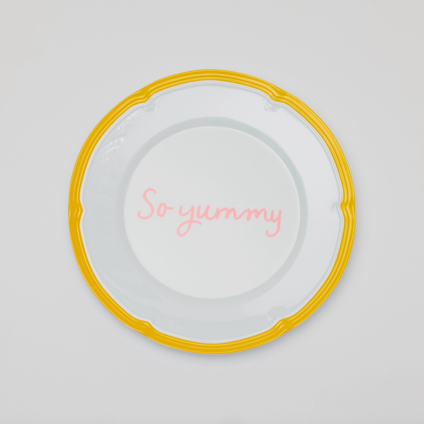A melamine plate with a yellow border and, "So yummy" written in pink cursive in the center. 