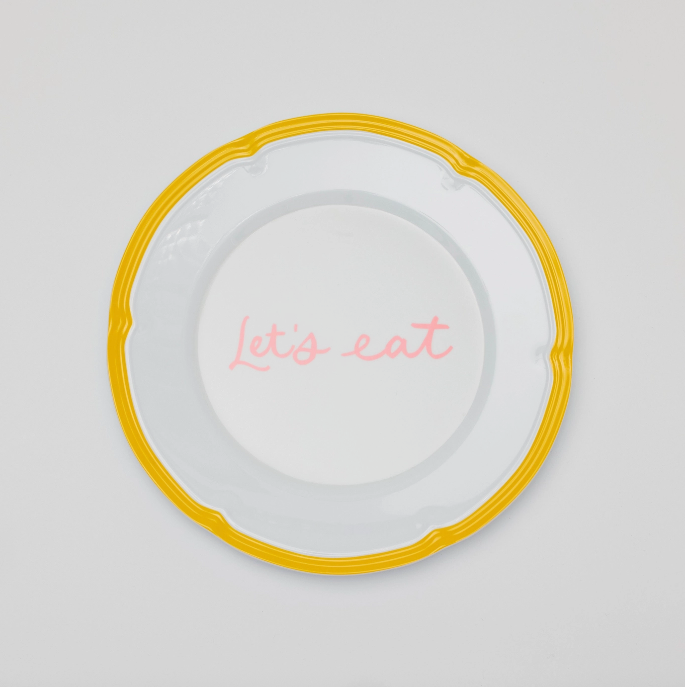 A white melamine plate with a yellow border and, "Let's eat" written in pink cursive in the center. 