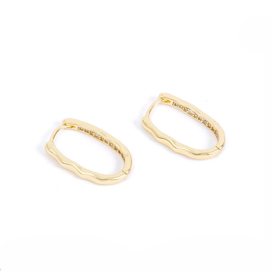 A pair of gold oval hoop earrings with a softly wavy edge are shown against a white background. The inside edge is lined with small sparkling stones, adding a subtle touch of shimmer to the modern design.