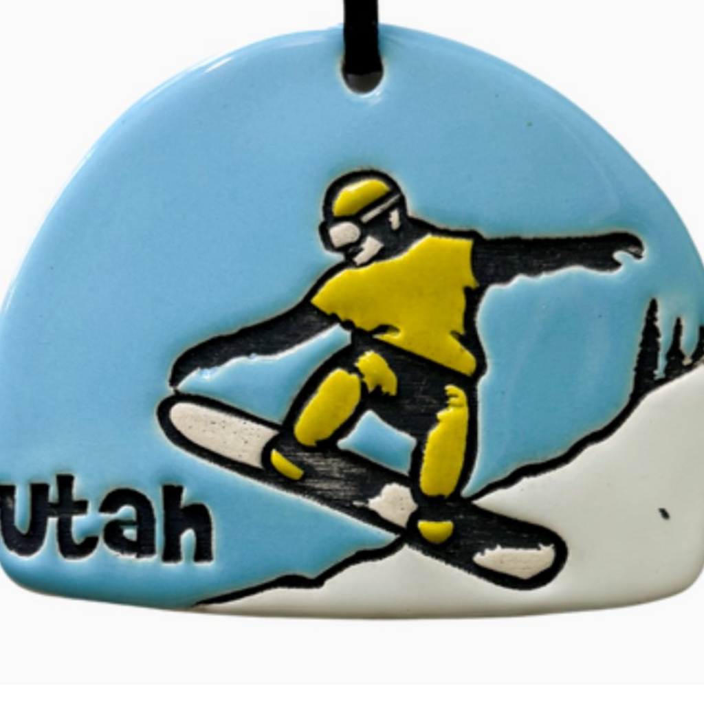 Ceramic ornament featuring a snowboarder pulling an ollie down the slope. 