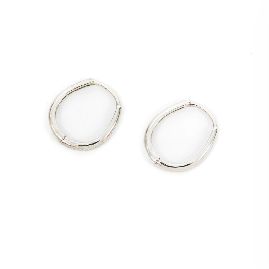 A pair of thin silver hoop earrings are designed in a slightly irregular oval shape, giving them a modern, organic feel. Their minimalist style makes them versatile for both casual and dressy outfits.