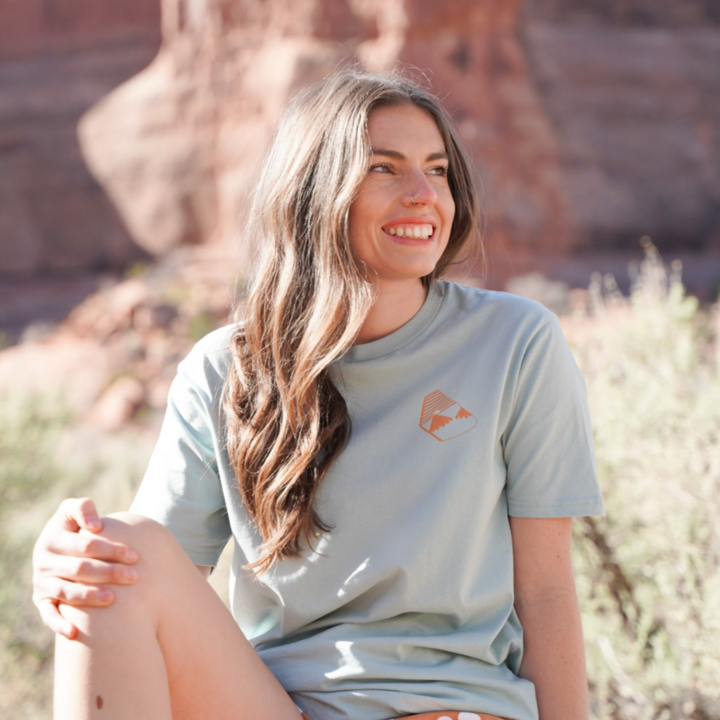 Blue and orange tee shirt. A pottery sherd decorates the front left chest. A dreamy how-to graphic with postcard feels adorns the back. Other hand-drawn highlights include a starry butterfly and Canyonlands National Park pictograph.
