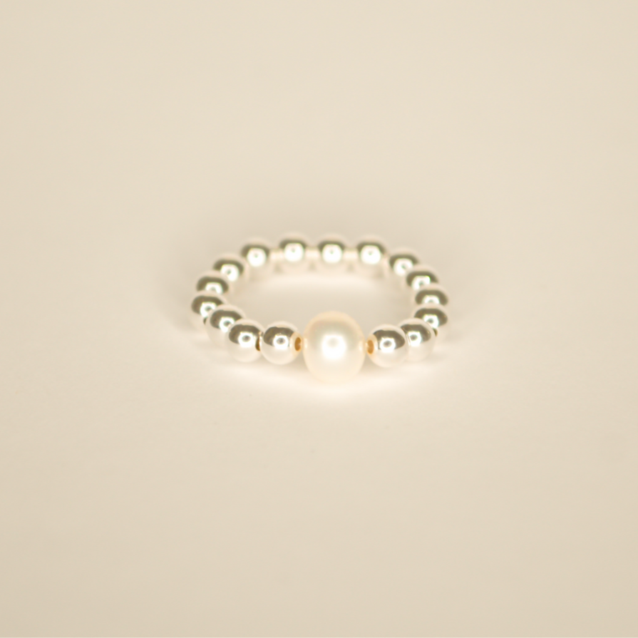 Silver beaded ring with a single large pearl bead. Pictured on an off white back ground.