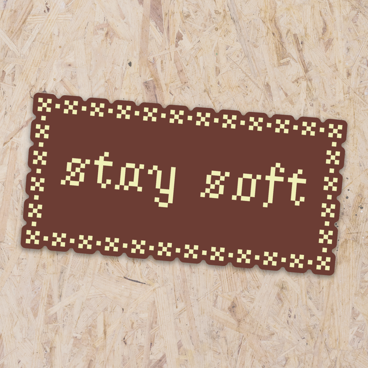 brown rectangle sticker with yellow cross-stitching details, reading "stay soft"