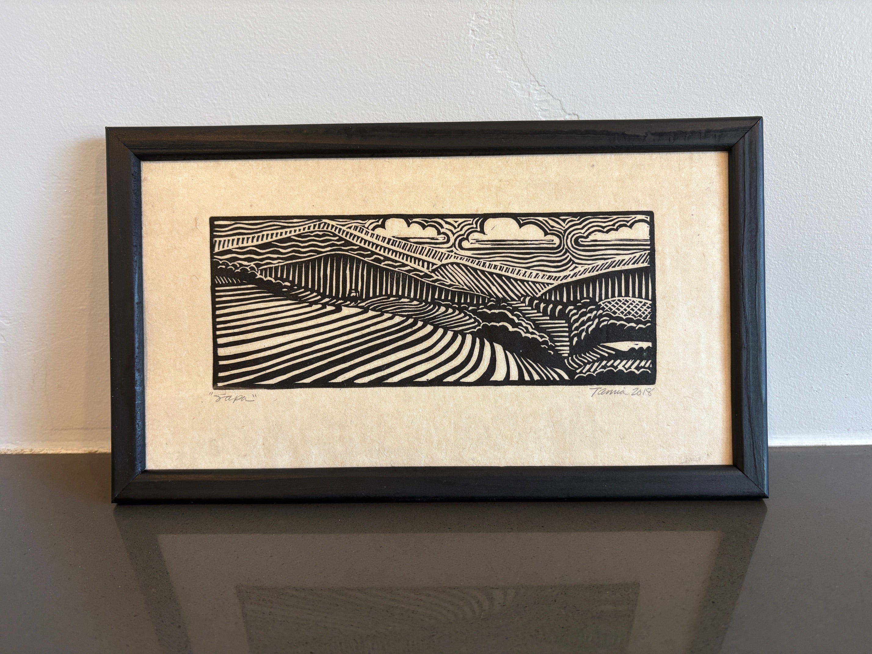 Linocut image of mountains, grass, and sky. Only black ink is used on an ivory colored paper. 