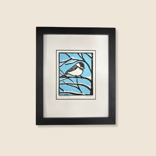 linocut on paper, Size is 9 x 11, little chickadee sitting on a thin branch, blue sky background, light snow falling and collecting the branches of the tree.