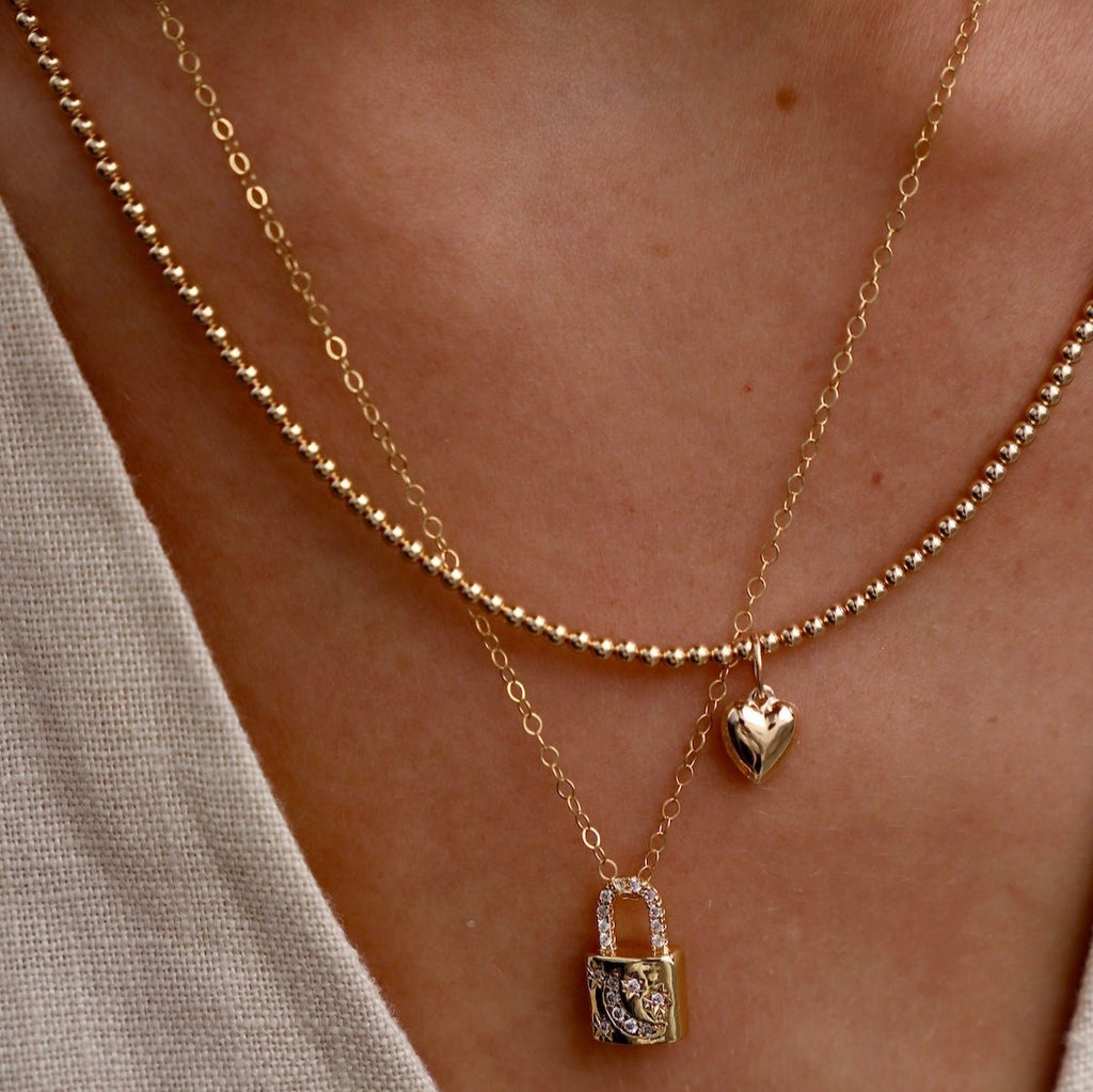 Add a touch of cosmic charm to your look with our Celestial Lock Charm Necklace. Crafted with a petite gold plate lock charm, accented with delicate cz star and moon embellishments. Perfect for adding a subtle, yet eye-catching detail to any outfit. Elevate your style with this enchanting accessory.