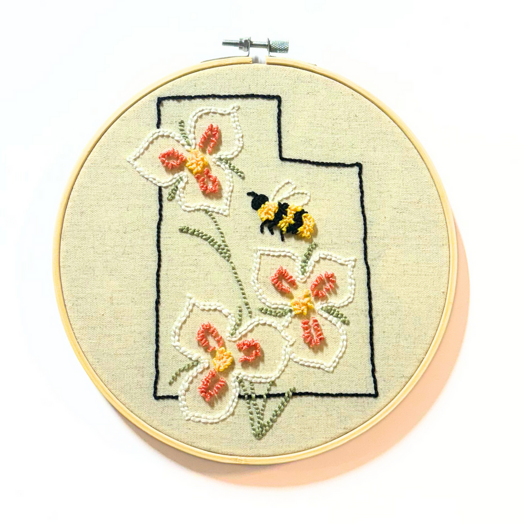 black outline of Utah with Sego Lilies and a bumble bee