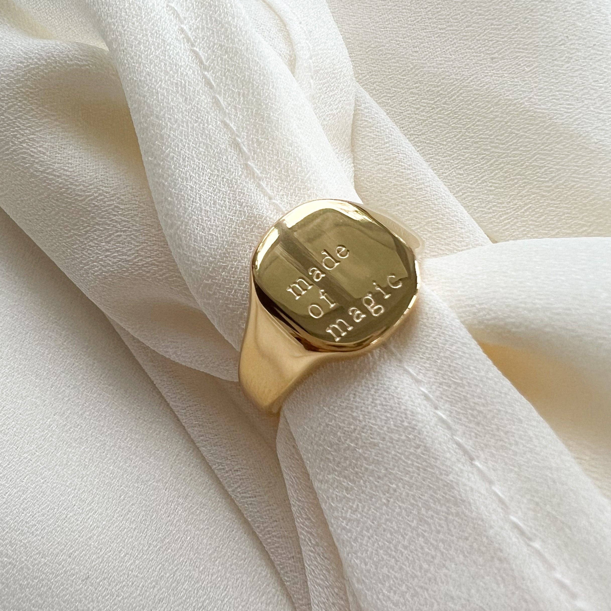 Gold ring with 'made of magic' engraving on a white fabric background
