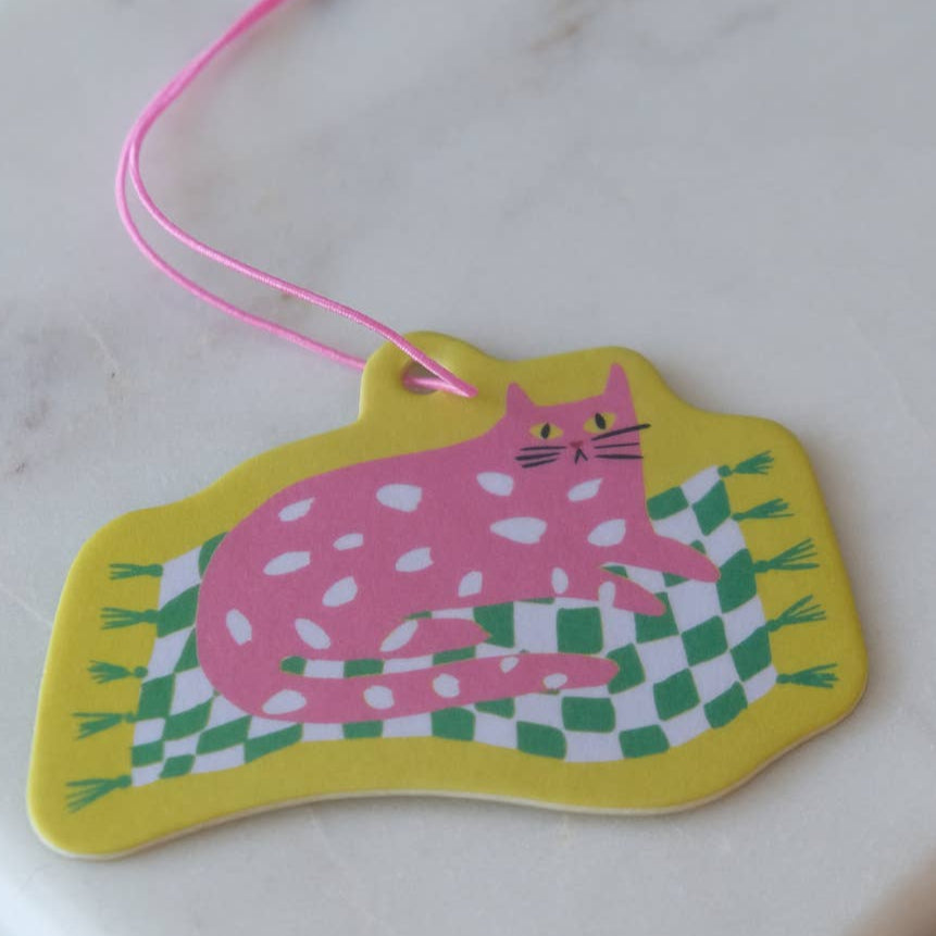 Colorful cat-shaped air freshener with a pink cat on a green and white checkered rug, attached to a pink string.